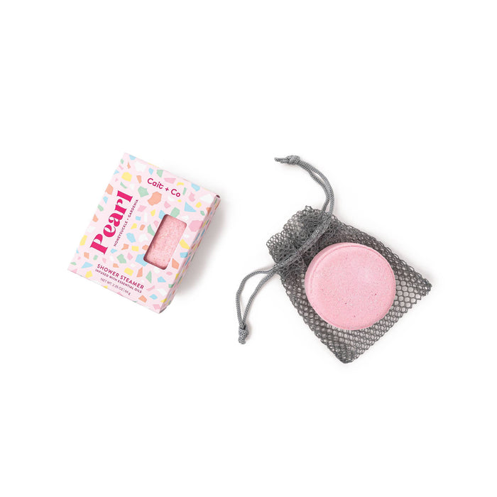 A pink shower steamer with a Gem Shower Steamer packaging and a black mesh bag, placed on a white background.
