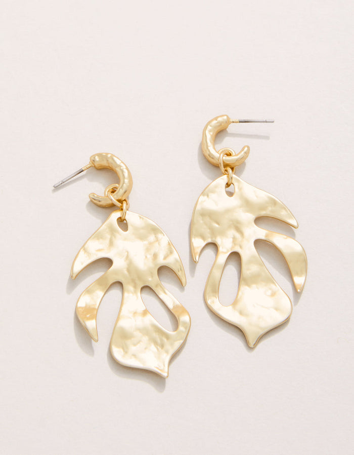 Gold leaf-shaped earrings on a light beige background