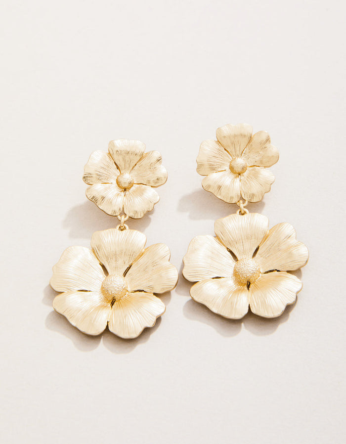 Gold floral earrings on a light beige background